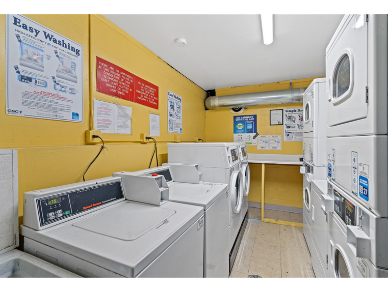 Community laundry room with stacked washing machines and dryers against yellow walls.