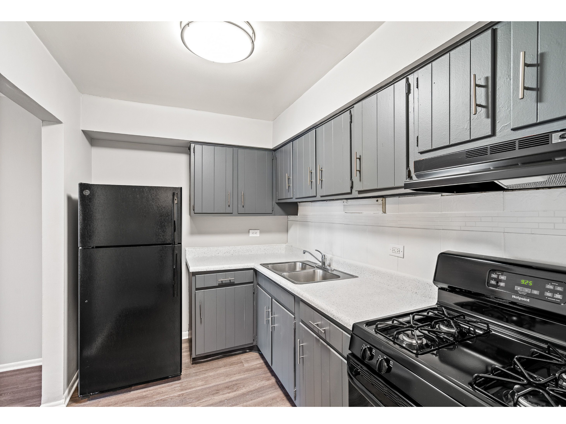 Modern apartment kitchen with gray cabinets, white countertops, sink, fridge, and stove.