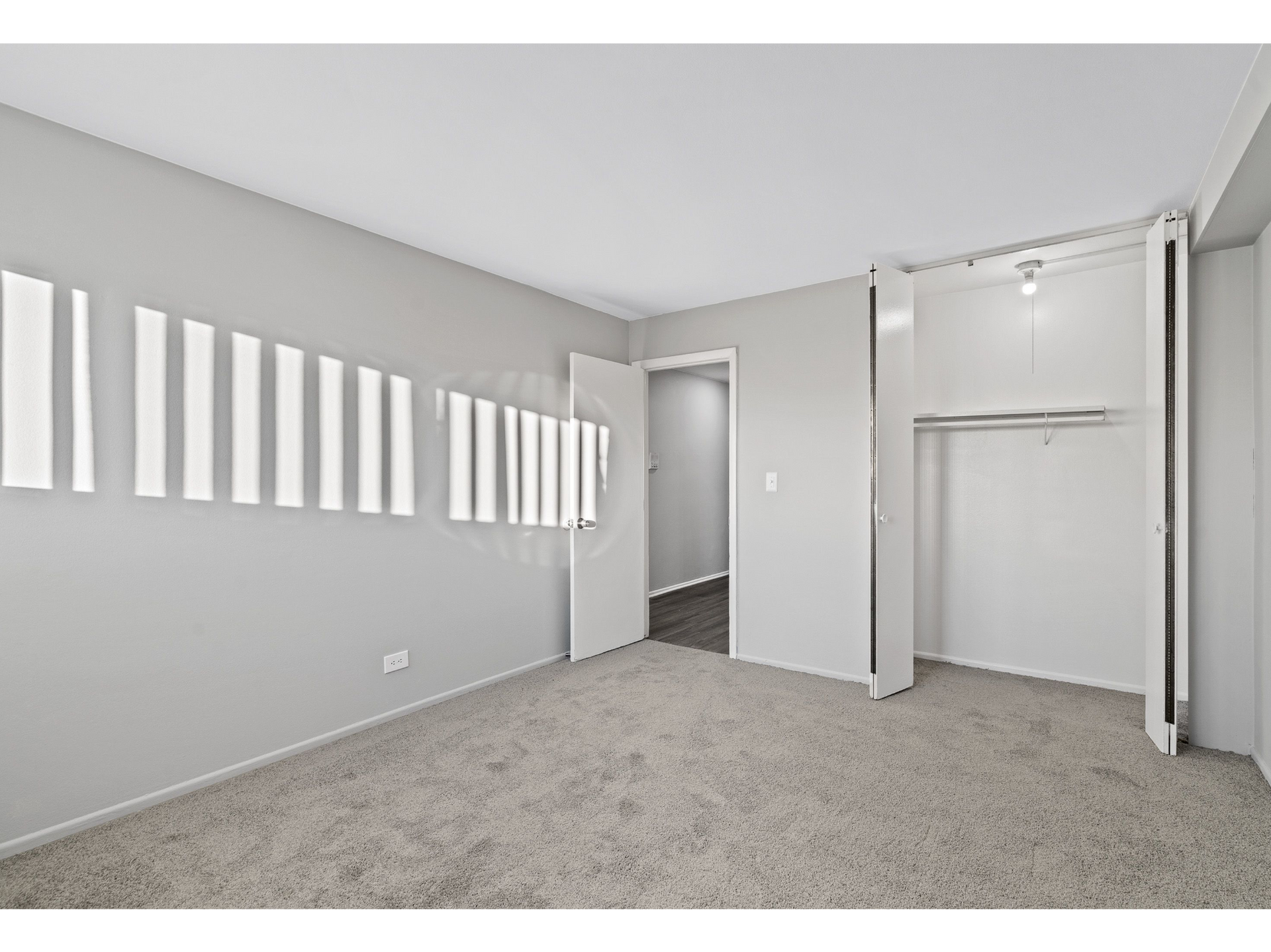 Empty bedroom with gray walls, beige carpet, and an open double-door closet.