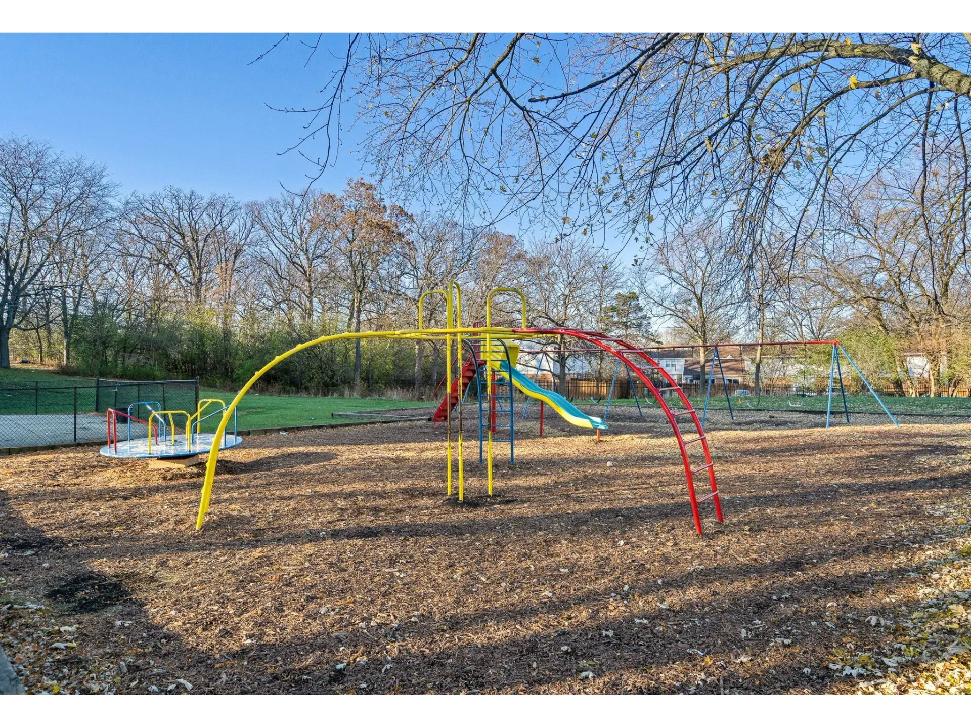 Colorful playground equipment with slides and climbing bars in a tree-lined park area.