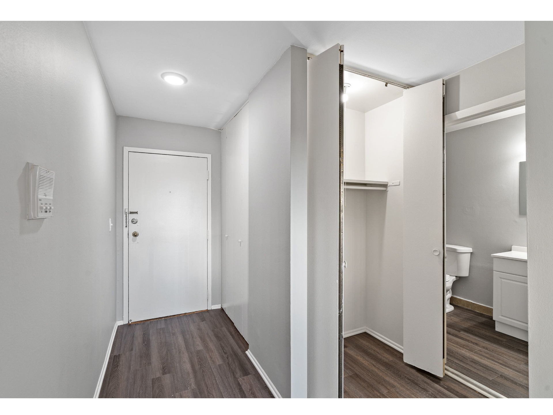 Hallway inside an apartment, showing entry door, open closet, and a bathroom.