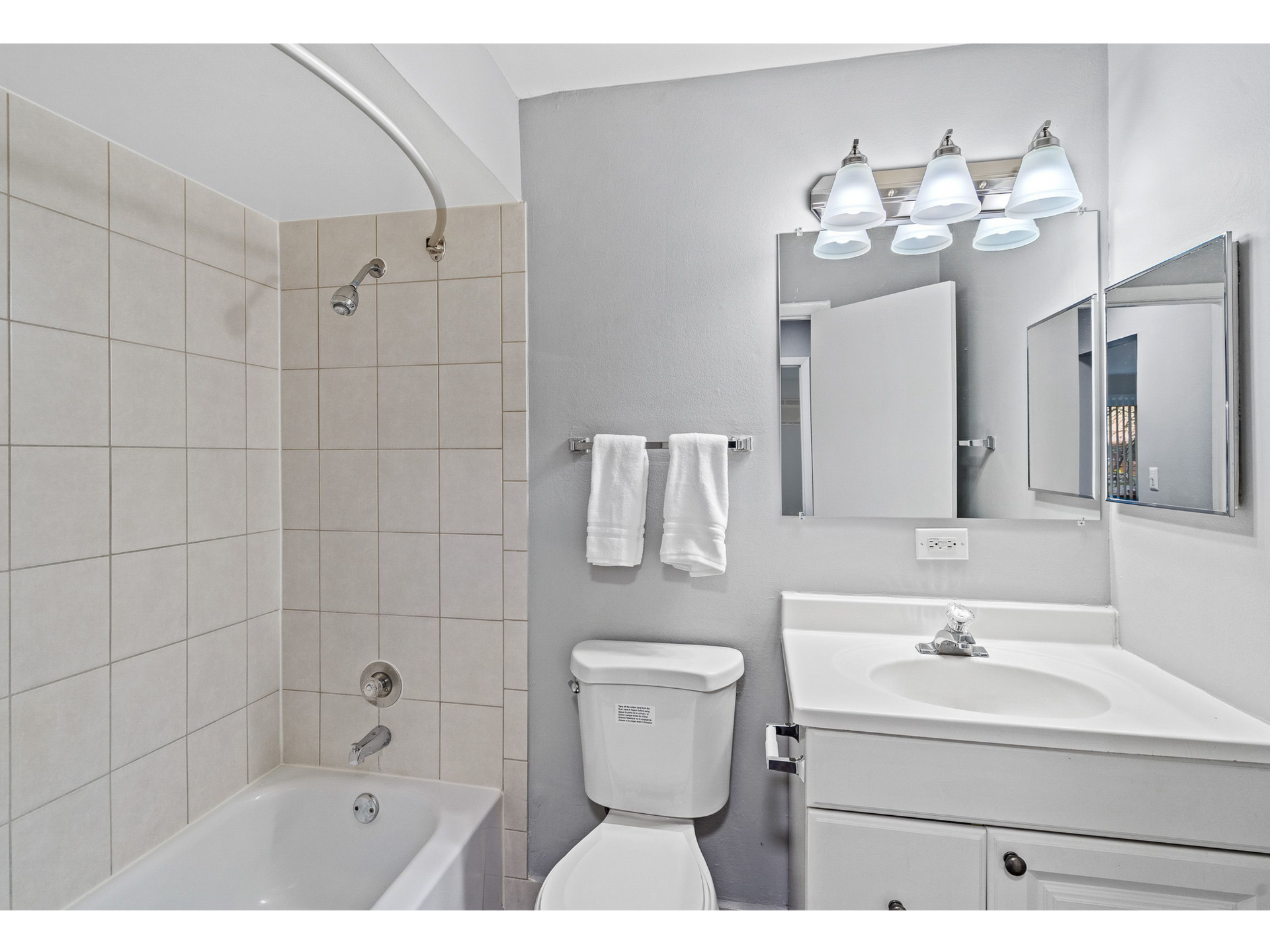 Bathroom in an apartment with tub/shower, tiled walls, toilet, and white vanity with mirror.