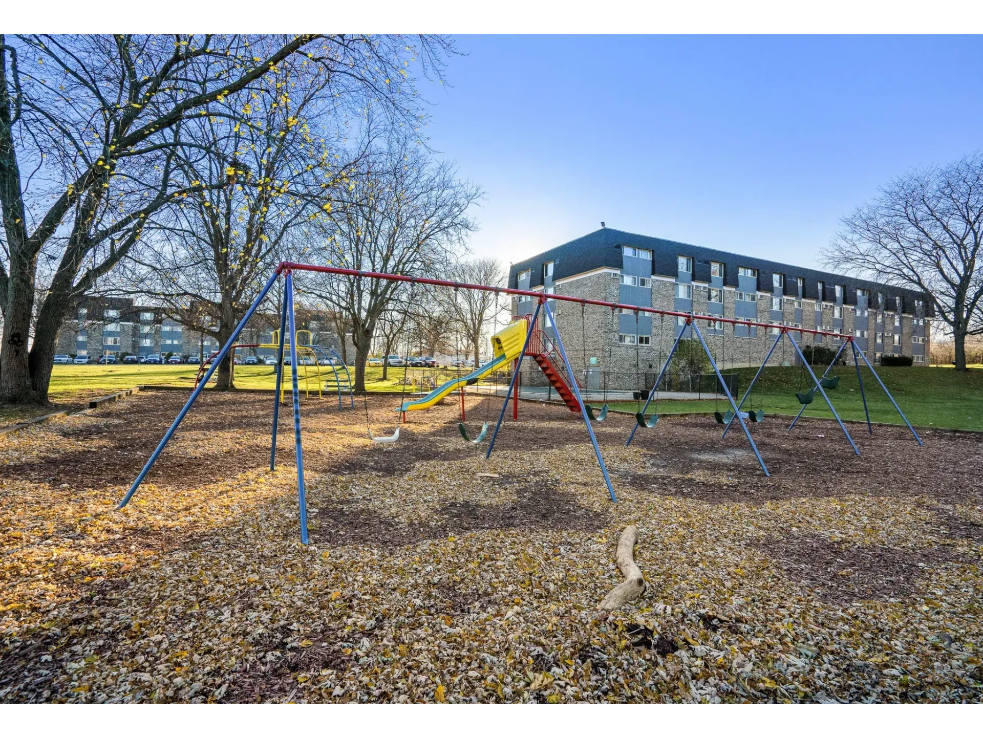 Playground with swings and a slide in a grassy community space beside an apartment building.