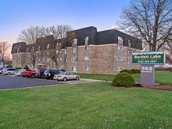 Exterior view of Bartlett Lake apartments with a parking lot and a property sign.