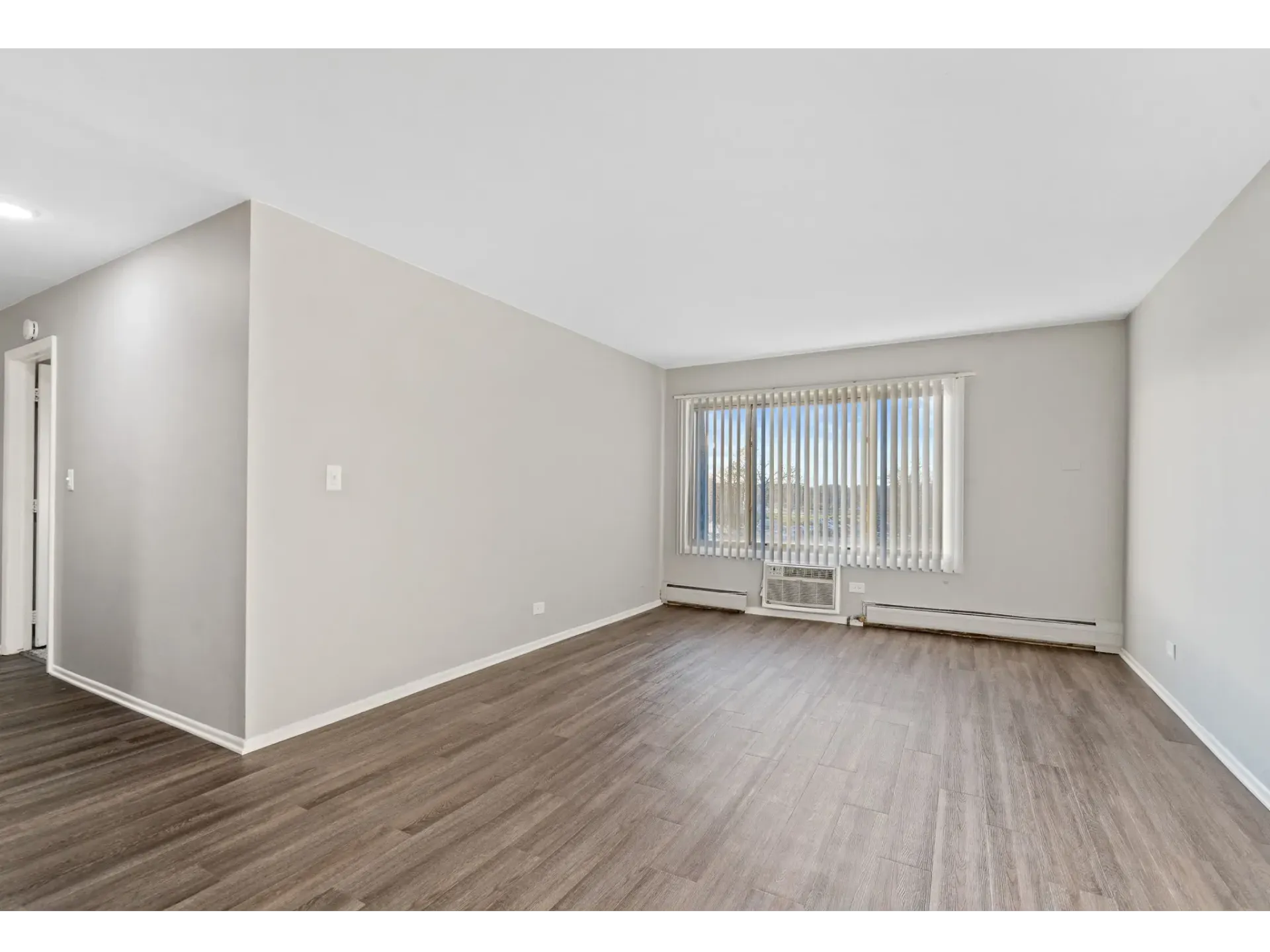 Empty apartment living area with large window and vertical blinds at Bartlett Lakes, offer apartments for rent in West Chicago, IL.