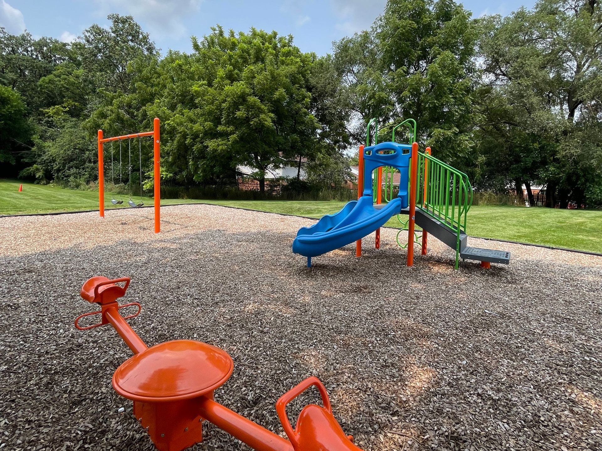 A playground with swings and a slide in a park, with an apartment building in the background. Autumn leaves on the ground.