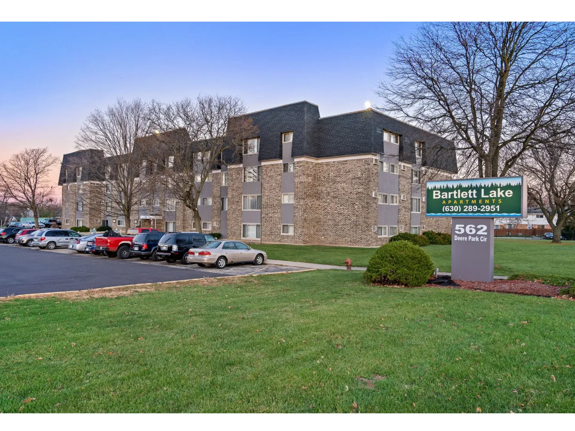 Exterior view of Bartlett Lake Apartments building with sign and parked cars.