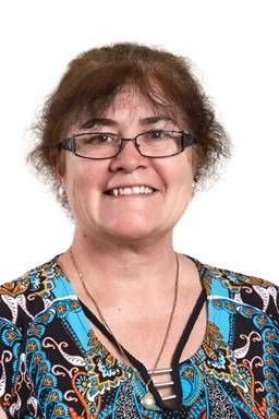 A person with shoulder-length brown hair and glasses, wearing a patterned blue, black, and white top, smiles at the camera — Money Spider Conveyancing In Katherine, NT