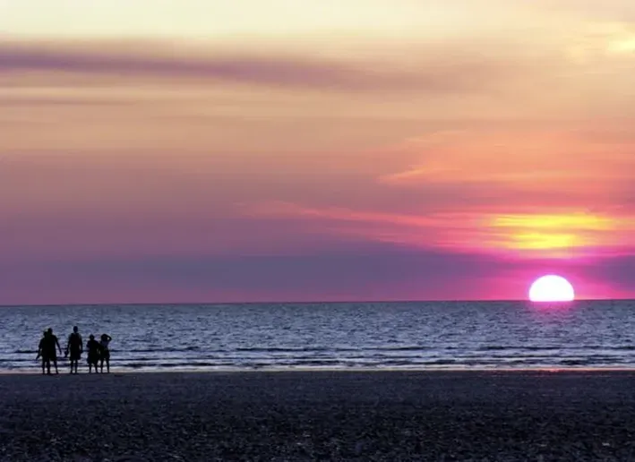 A vibrant sunset over the ocean, with the silhouettes of five people standing on the sandy beach shoreline — Money Spider Conveyancing In Katherine, NT