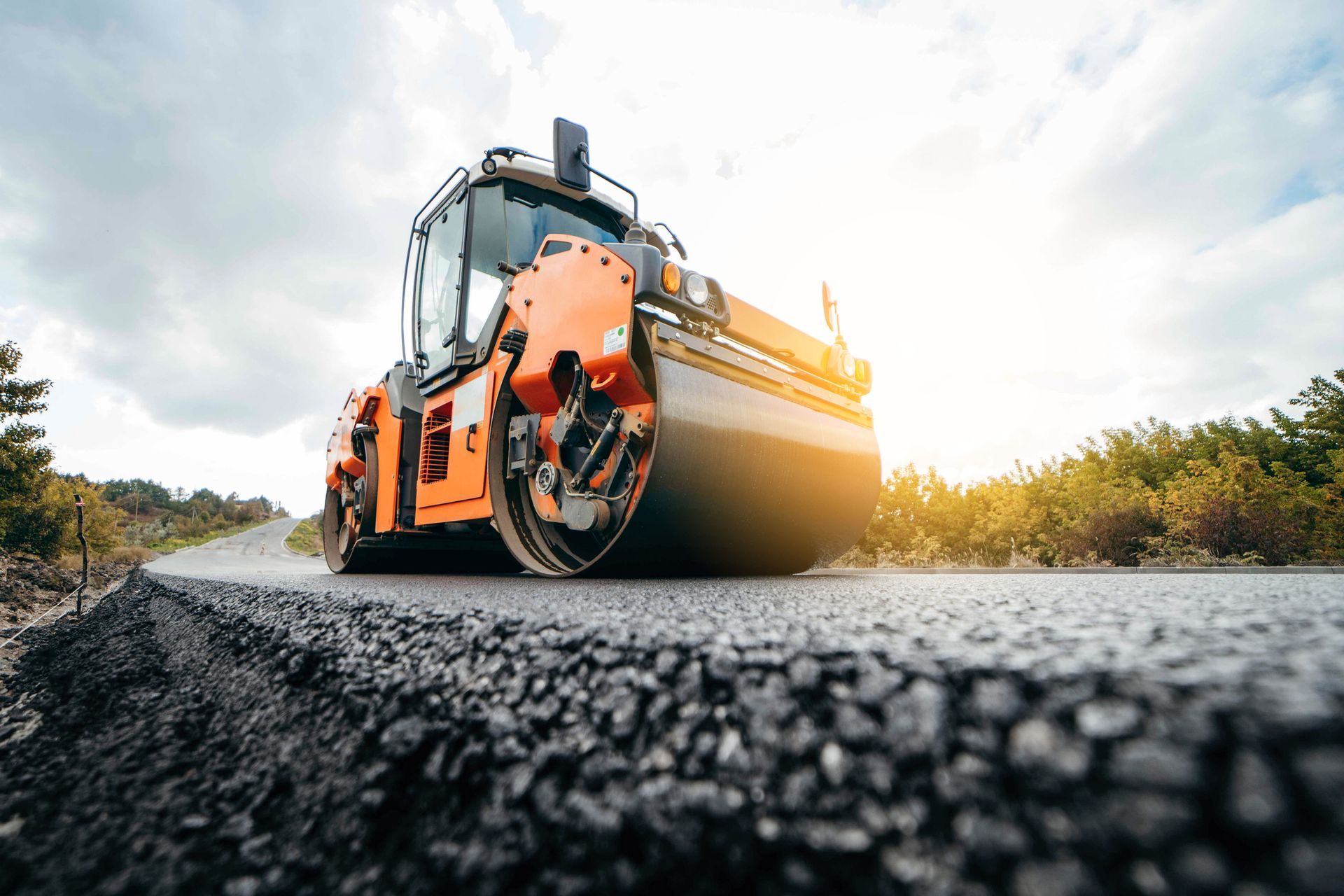Picture of a large commercial Roller flattening a asphalt surface. You can see a yellow rolller making asphalt road flat.