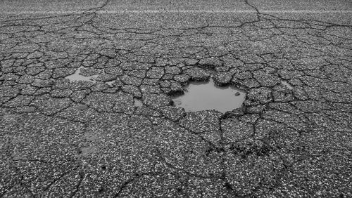 Pictutre of a pothole in a commercial parking lot. You can see a cracked asphalt parking lot with a pothole full of water in center.