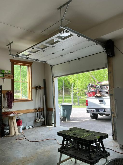 Garage door opening, revealing a truck and backyard. White door, grey concrete floor, work table in front.