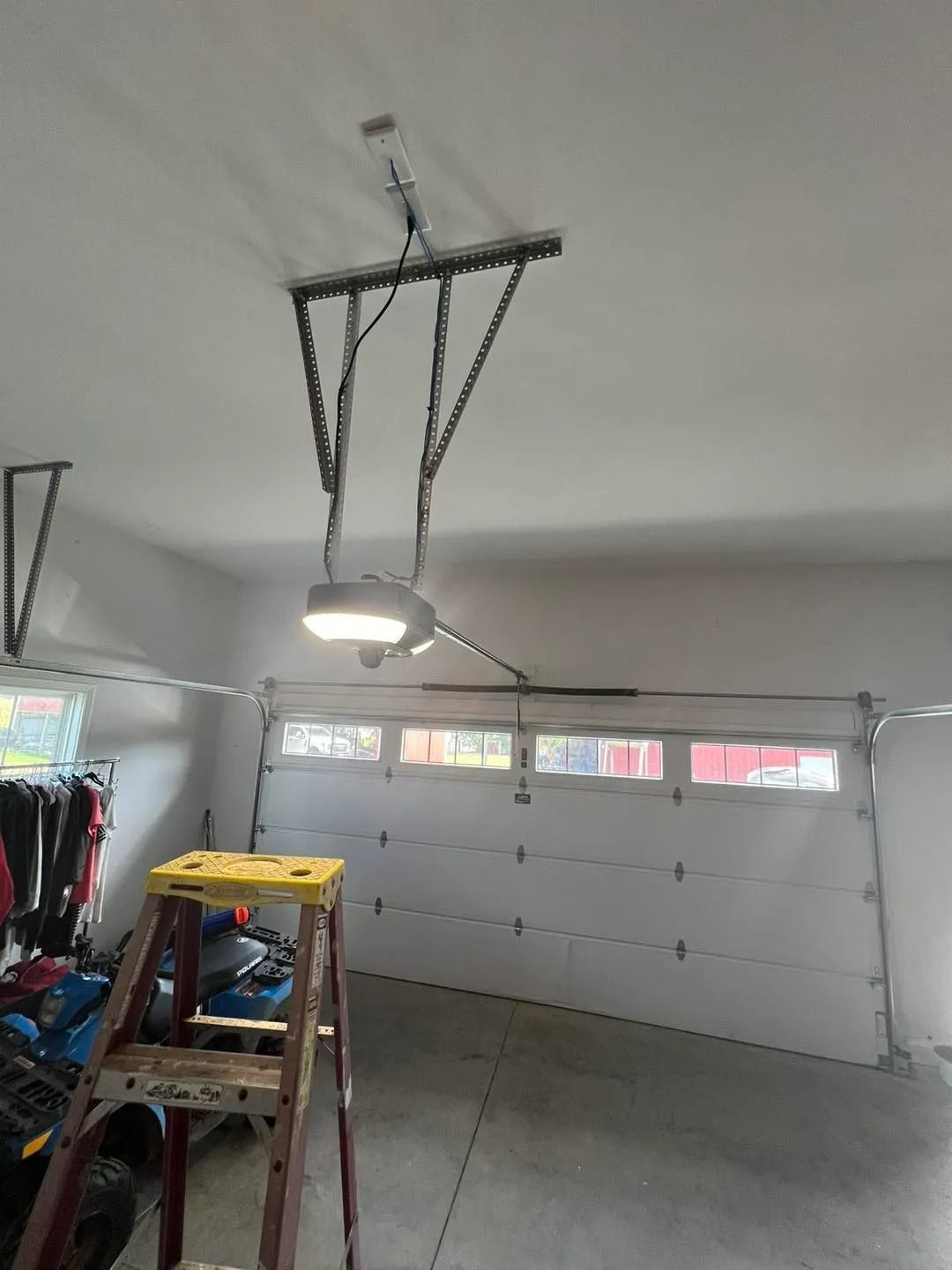 Garage interior with a ladder. Garage door is white. Garage door opener hanging from the ceiling.