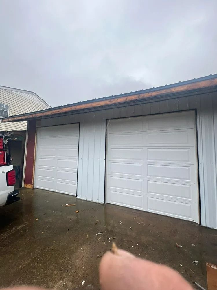 Two white garage doors on a white metal building under an overcast sky.