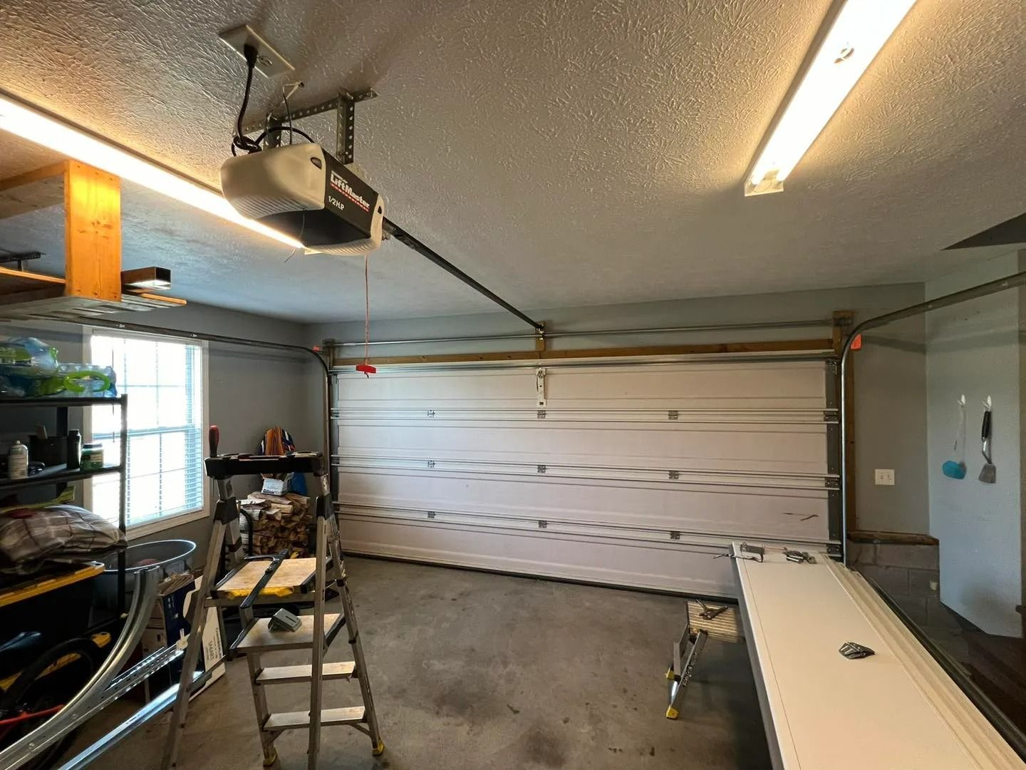 Garage interior with closed white garage door, opener, shelving, and a ladder.