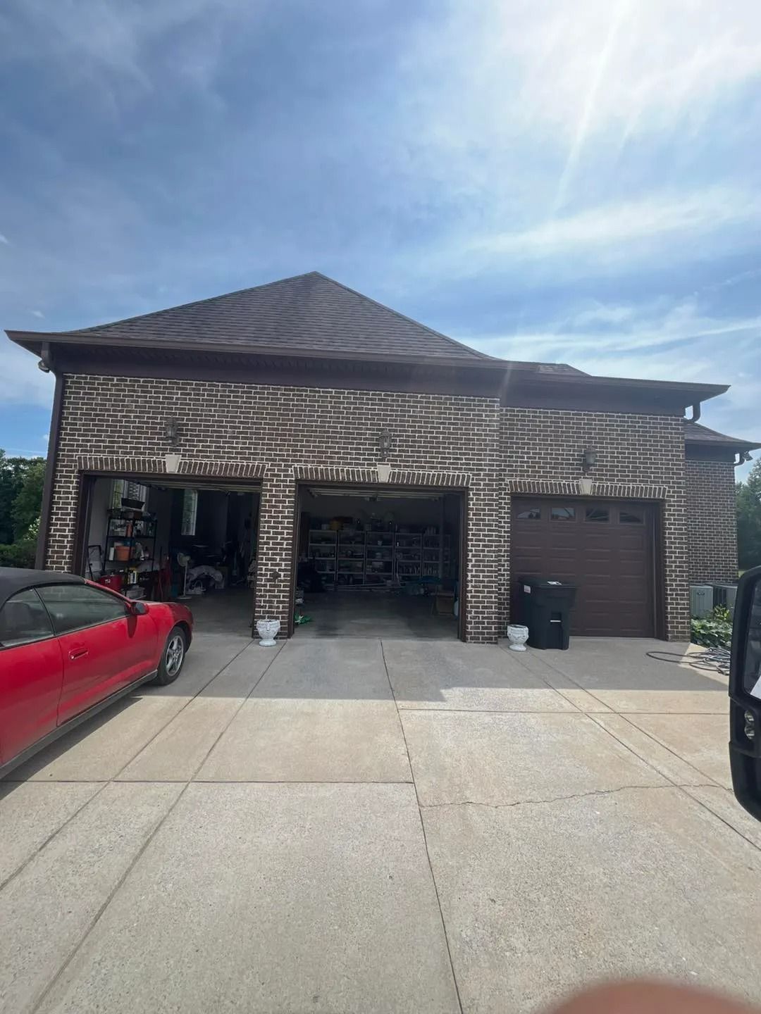 Brick garage with three bays, red car, and dark brown roof on a sunny day.