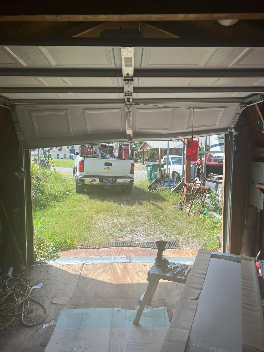 Damaged garage door open to show a white truck outside. Green grass and other vehicles visible.