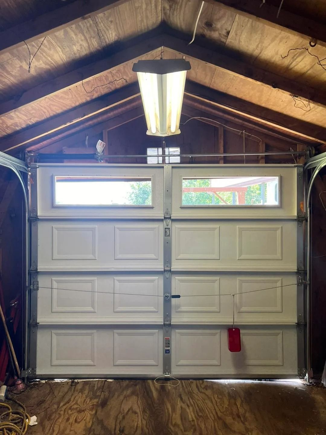 Closed white garage door with two rectangular windows above the panels, light fixture hangs from the ceiling.