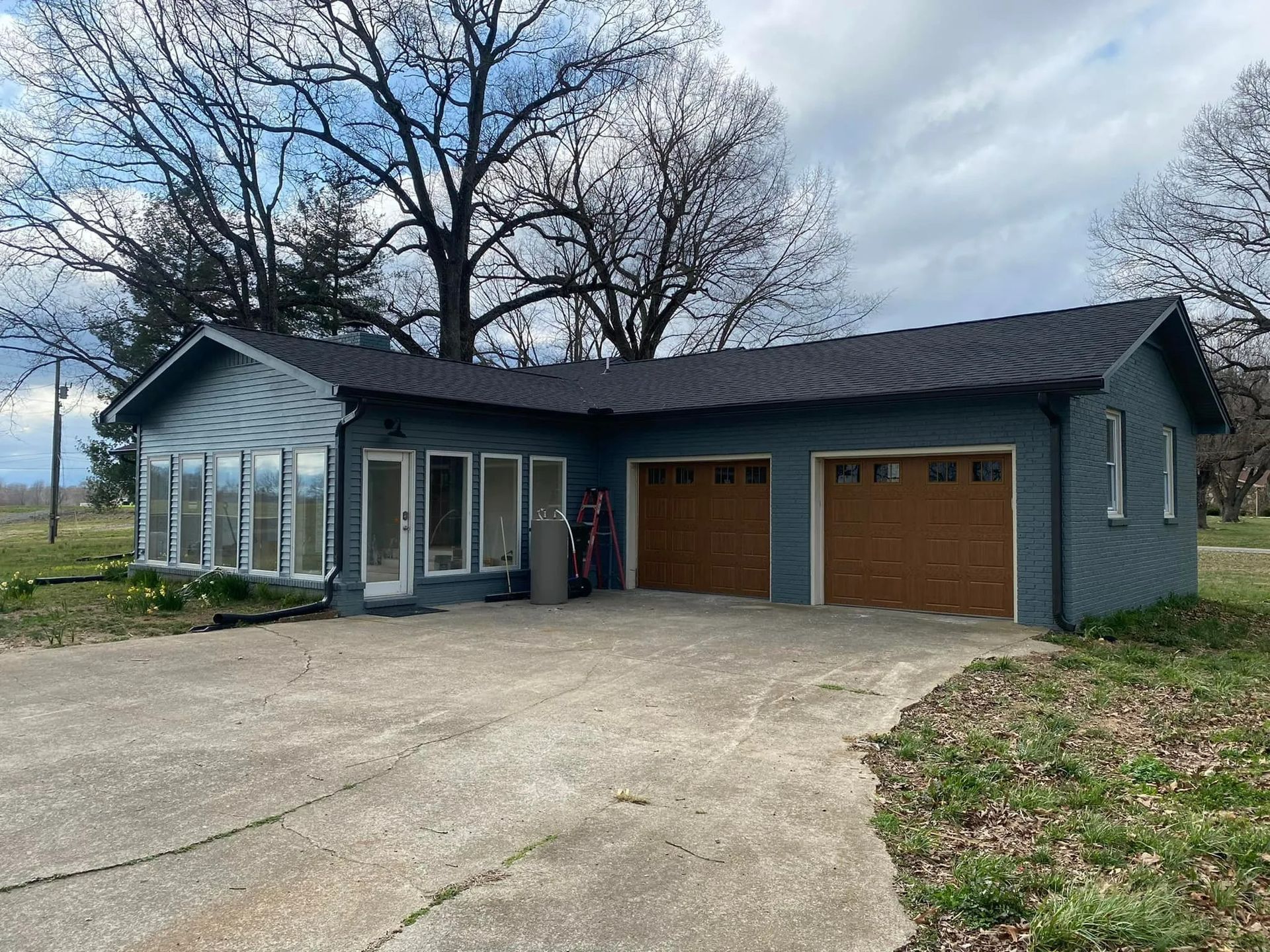 Blue building with brown garage doors and a sunroom, concrete driveway, trees in background.