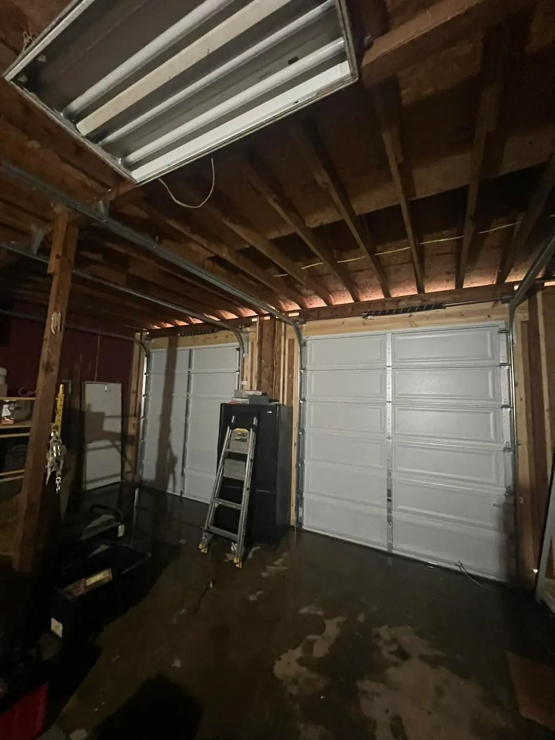 A garage interior with two white garage doors, exposed wooden beams, and a ladder.