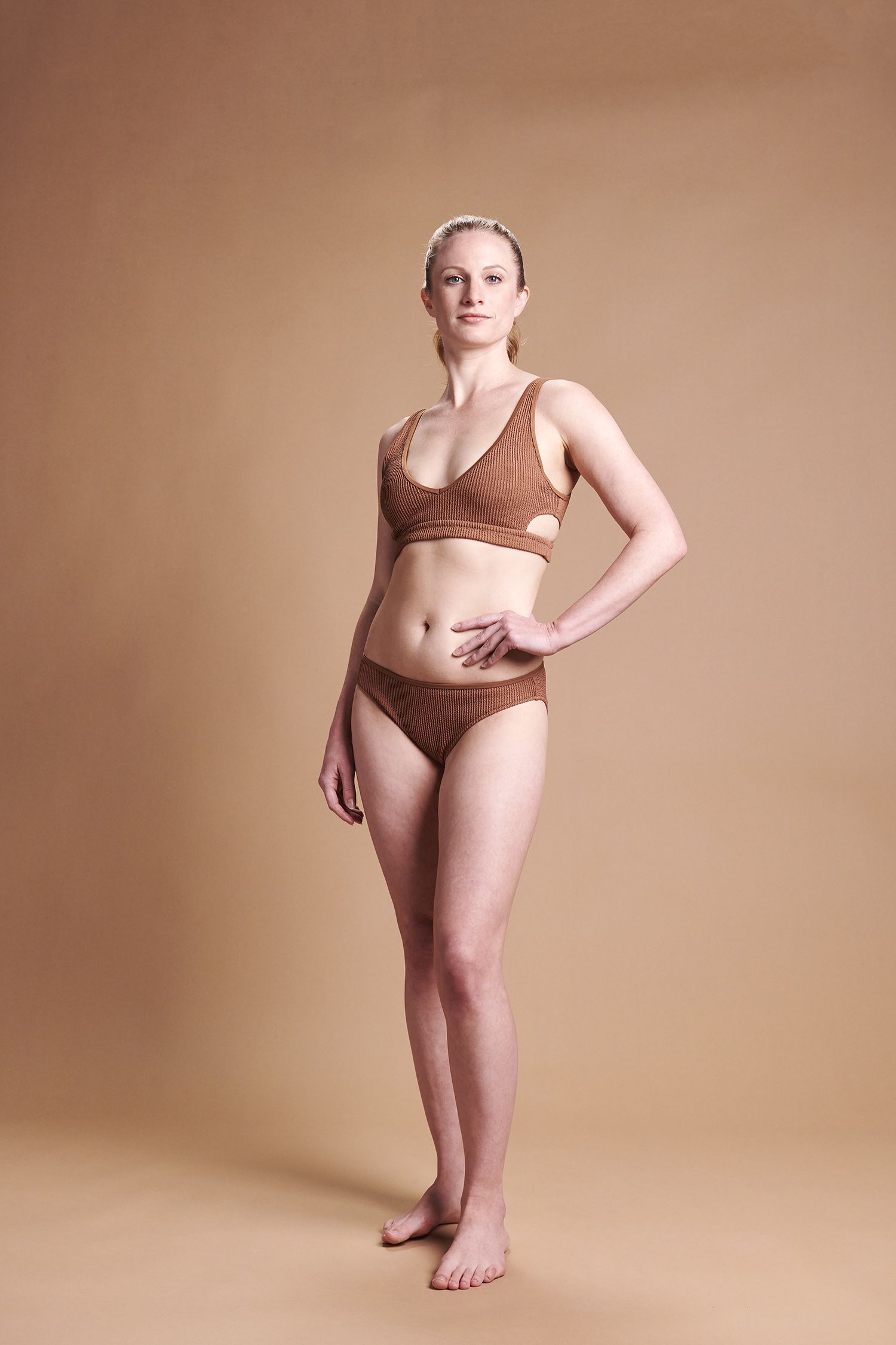A woman in a bikini is standing in front of a brown background.