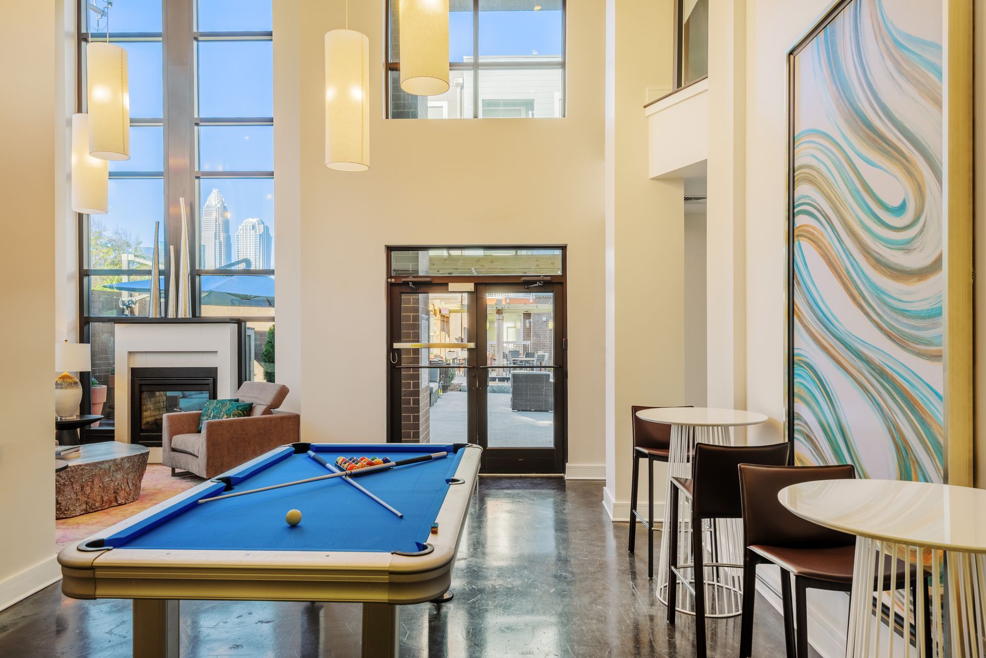 An upscale lounge with a blue pool table, bar stools, large windows, and an abstract artwork.