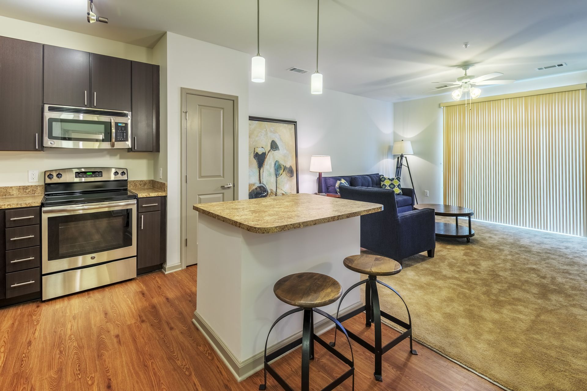 Modern open-concept kitchen and living area with island, stools, and dark cabinets.