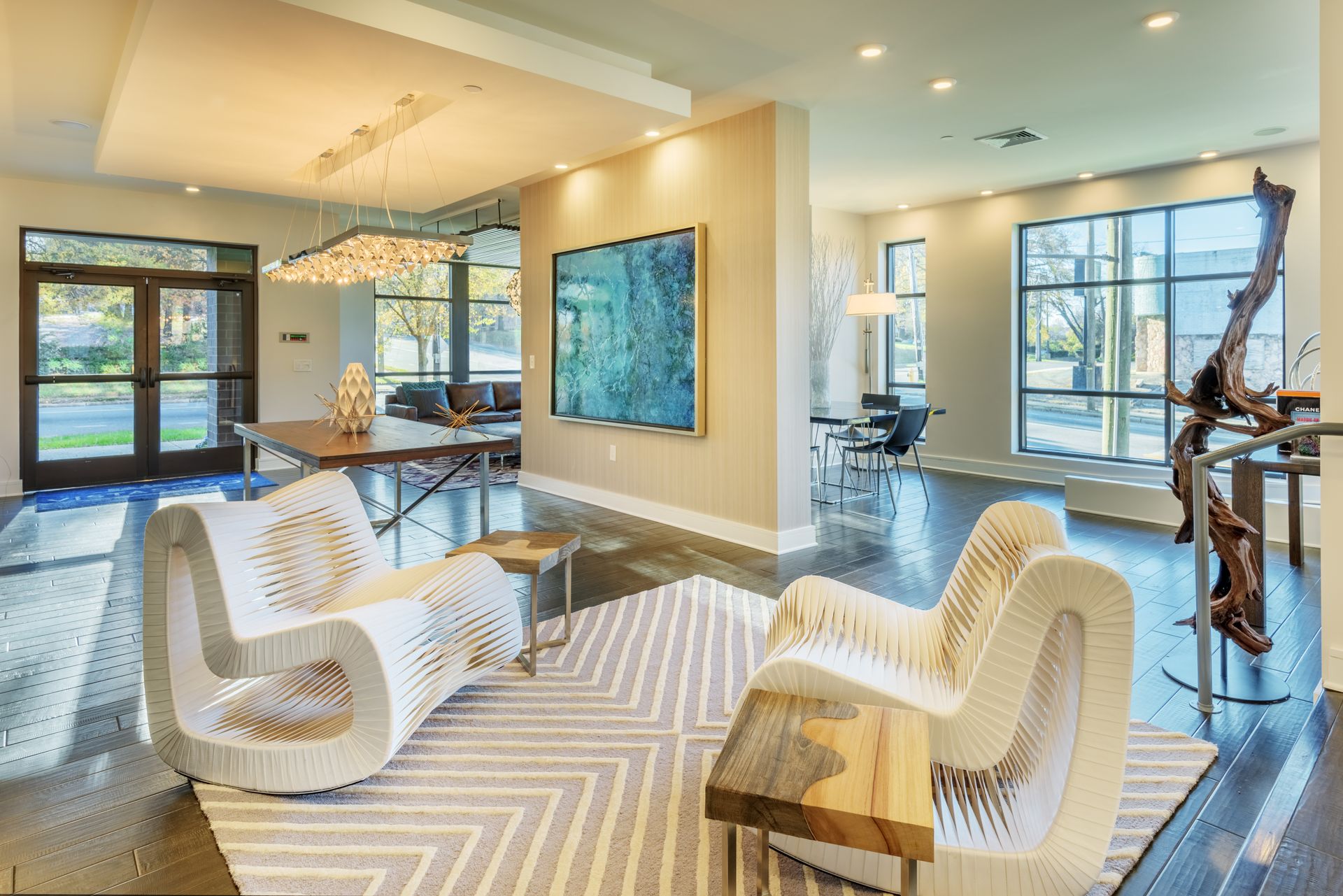 Modern lounge with white chairs, rug, artwork, and large windows.