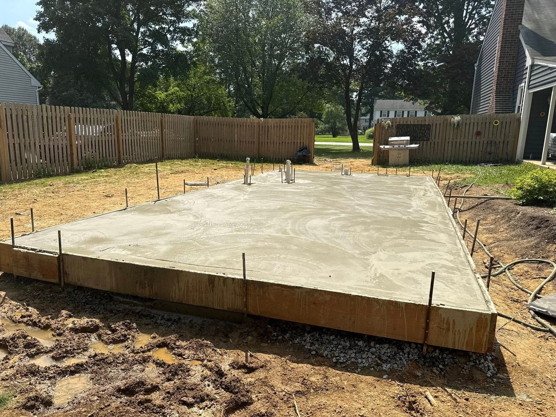 Fresh concrete slab foundation in a fenced backyard with wooden forms and construction tools