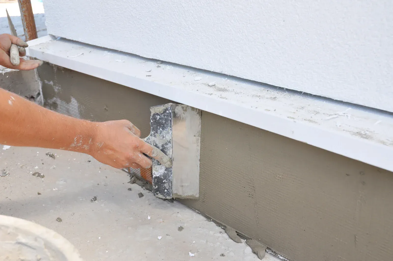Person applying plaster to a wall base with a trowel outdoors