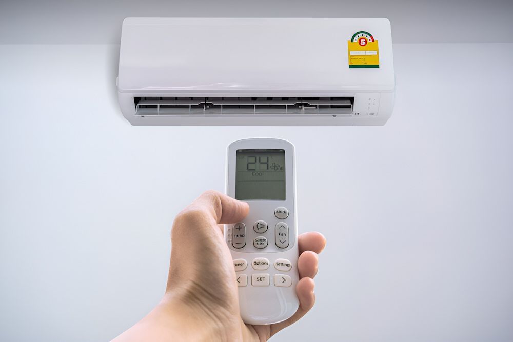 A Person Is Holding A Remote Control In Front Of An Air Conditioner — Mason's Air Conditioning Pty Ltd in Highfields, QLD