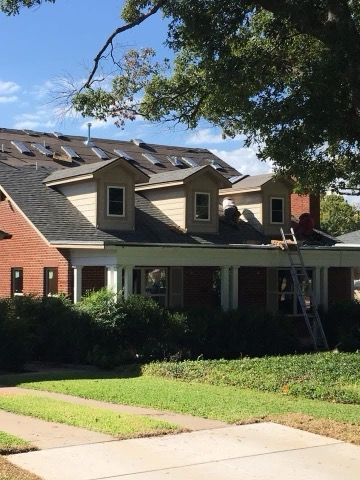House with roof partially under construction; workers on roof, ladder present, green lawn.