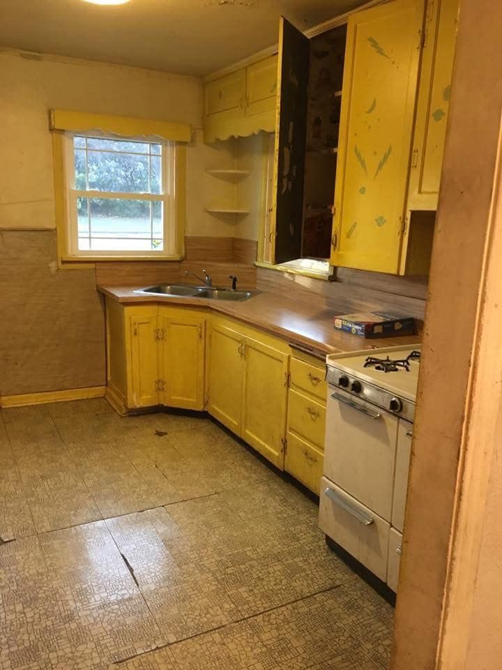Yellow kitchen cabinets and stove, with a sink, counter, and window; drab flooring.