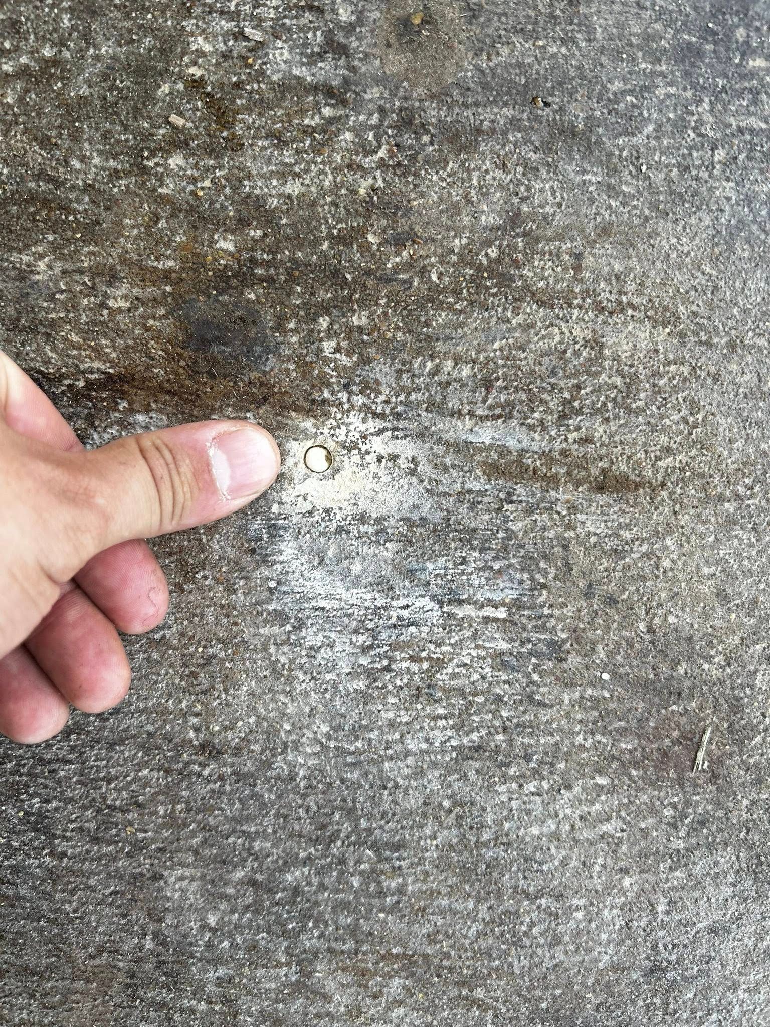 Hand pointing at a white scratch on a textured, gray surface.