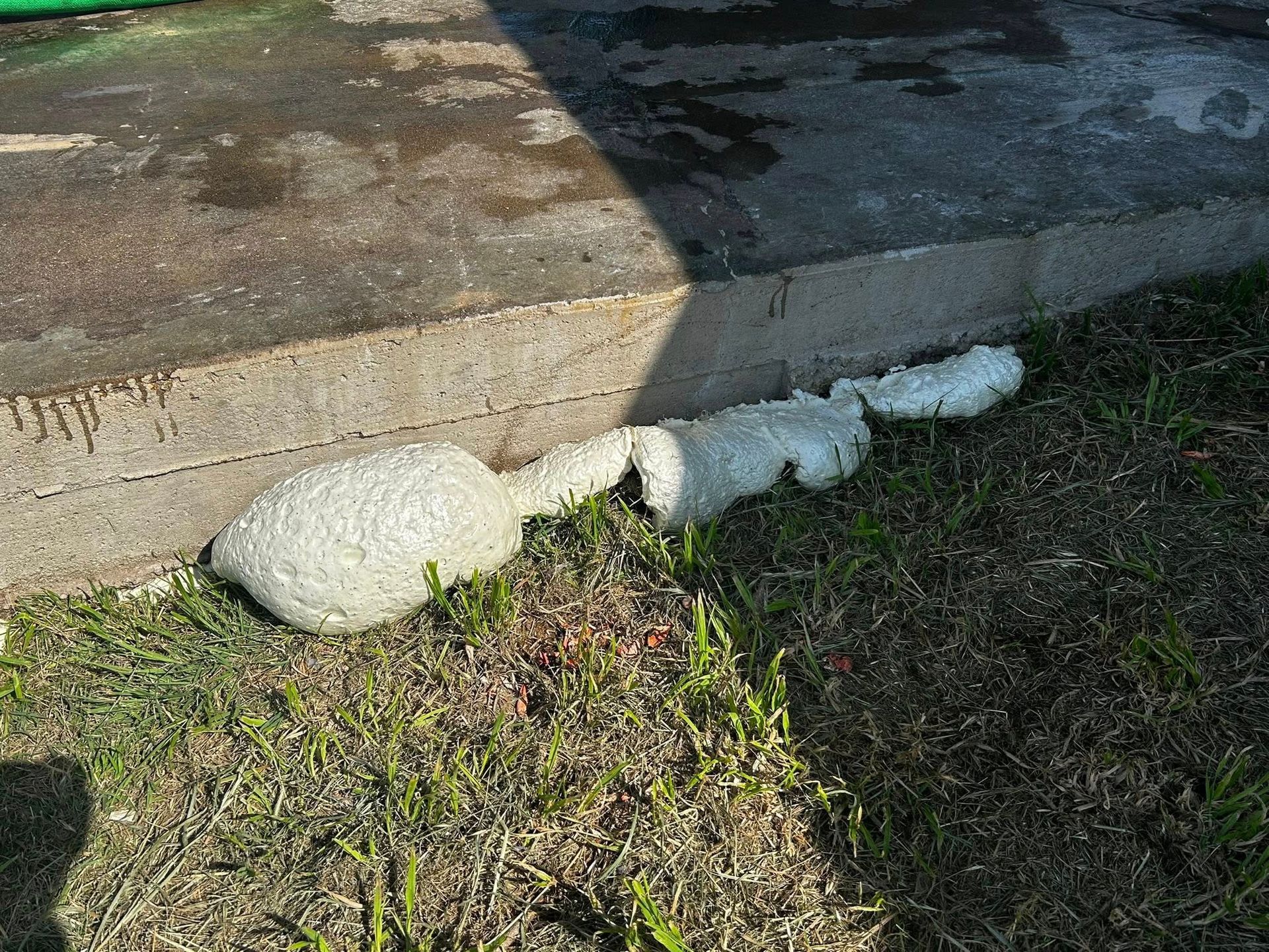 A large, blobby mass of concrete on grass next to a concrete step.
