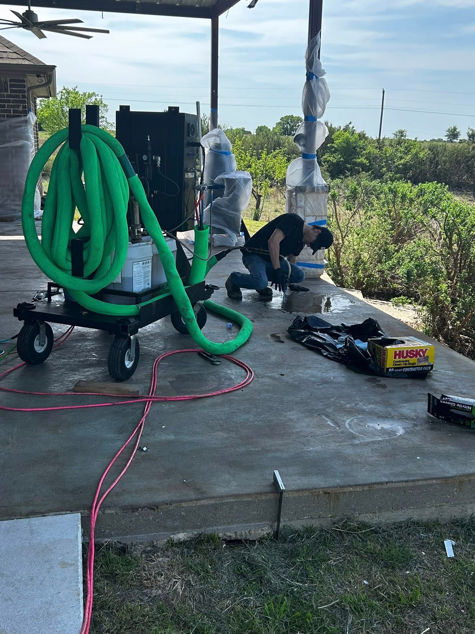 Person working on equipment next to a green hose cart under a covered patio.