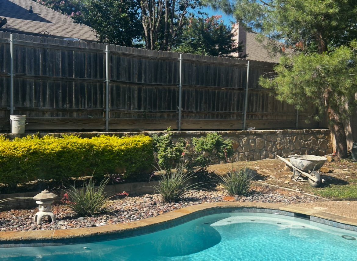Backyard with pool, wooden fence, greenery, and a small garden, on a sunny day.