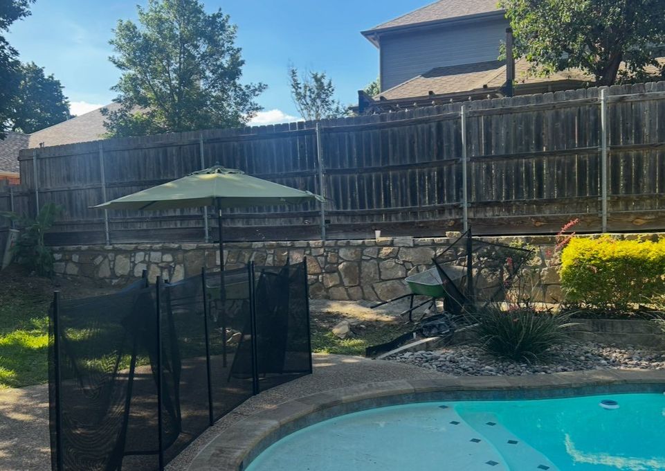 Backyard with pool, wooden fence, and green umbrella.