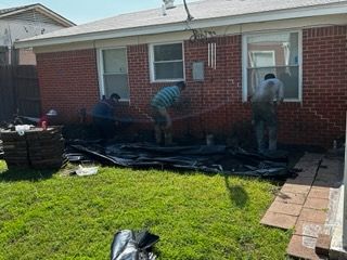Three workers install landscaping along a red brick building with grass in the foreground.