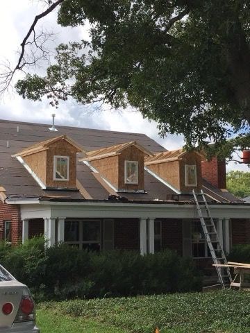 House with three dormers under construction; a ladder leans against the roof.