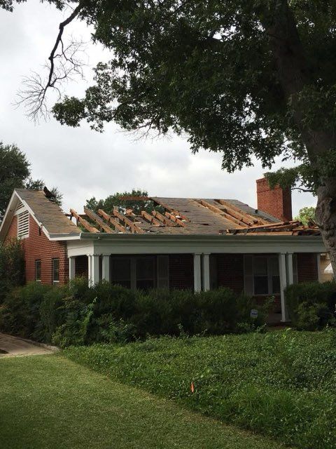 House with damaged roof after a storm; red brick, green foliage, gray sky.
