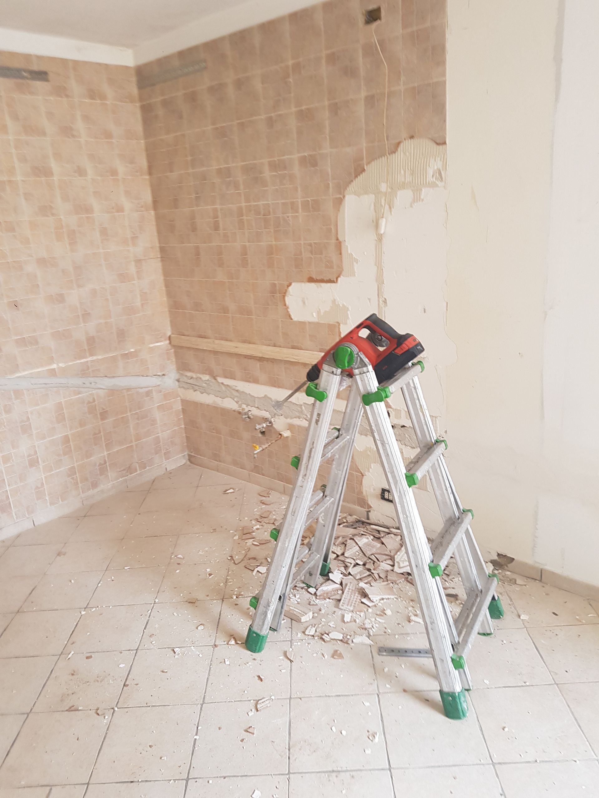 Ristrutturazione in corso: una scala con un attrezzo si trova in una stanza con piastrelle parzialmente rimosse sul muro.