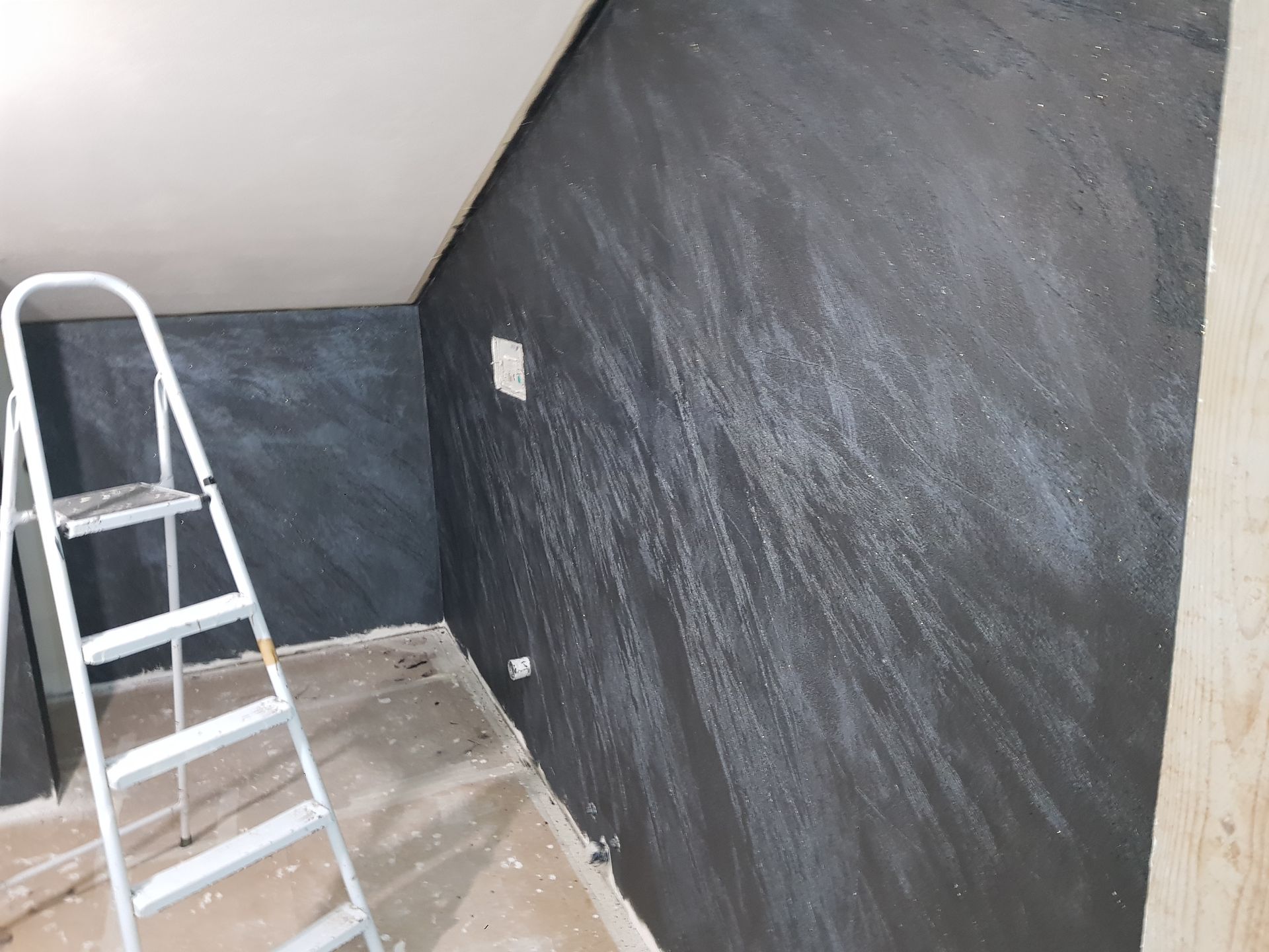 Stanza interna con parete dalla texture scura, scala e soffitto grezzo.