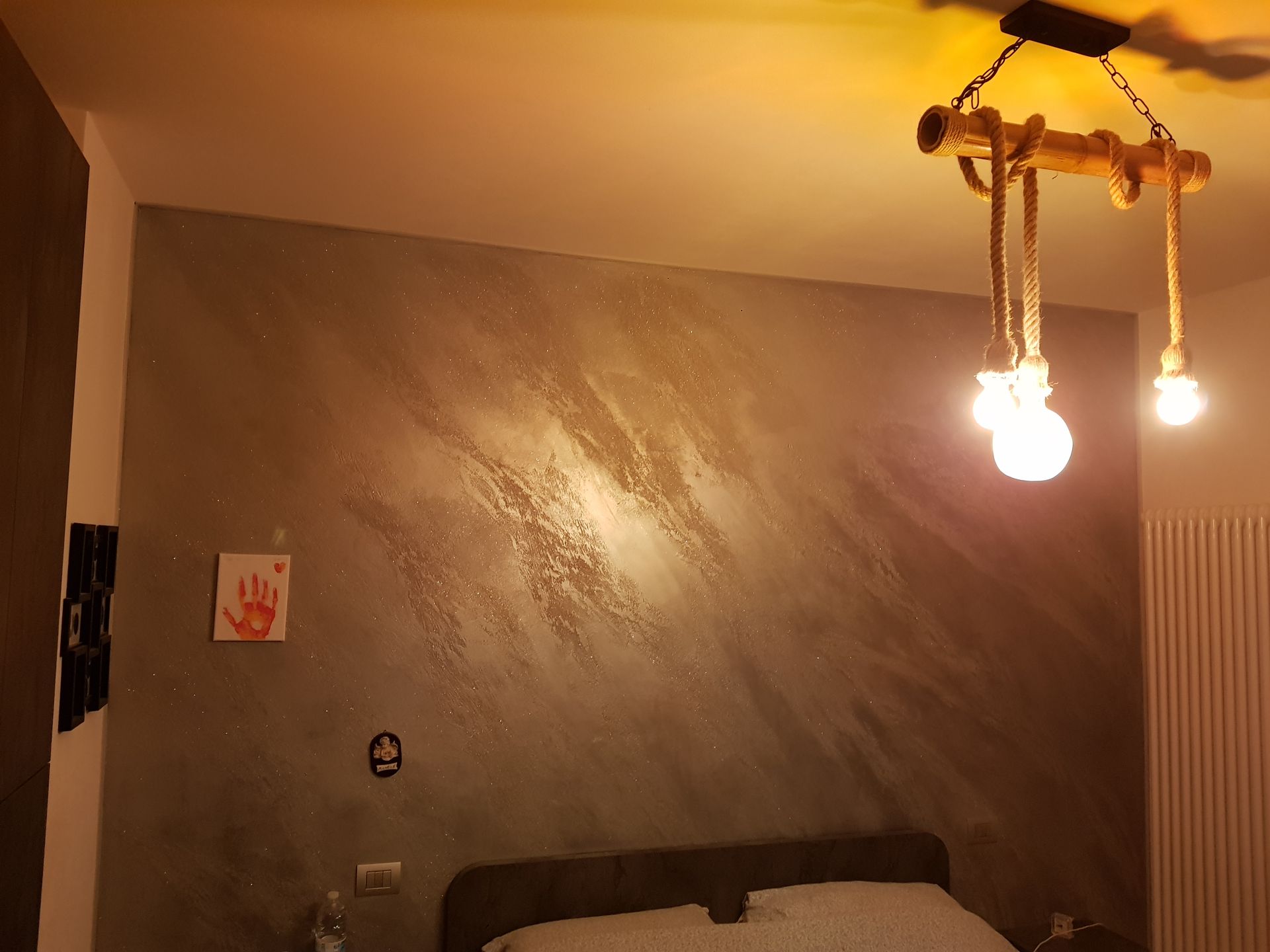 Camera da letto con parete grigia testurizzata, lampada rustica e letto.