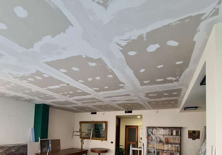 Soffitto con pannelli in cartongesso e stucco, stanza con mobili e porta.