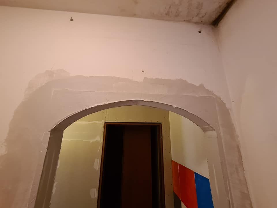 Arco in costruzione, appena intonacato, con un'apertura ad arco che conduce a un corridoio.