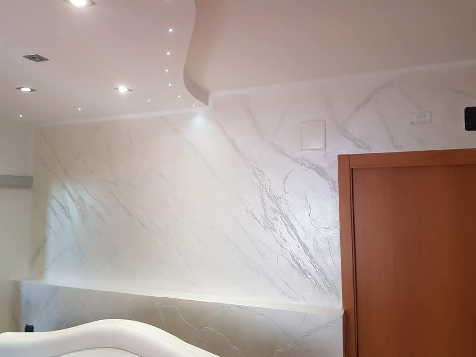 Parete effetto marmo bianco con striature, illuminazione da incasso e porta marrone.