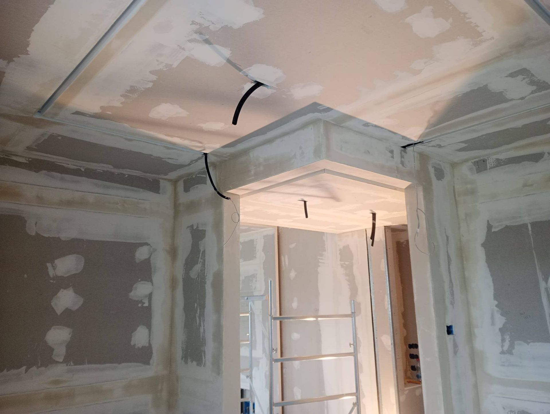 Interno in costruzione; cartongesso e struttura non finiti attorno a un'apertura, con cavi elettrici visibili.