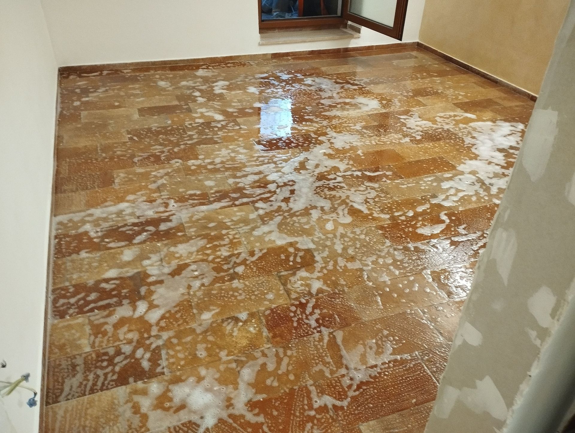 Pavimento in legno ricoperto di acqua saponata. Angolo di una stanza con una finestra visibile.