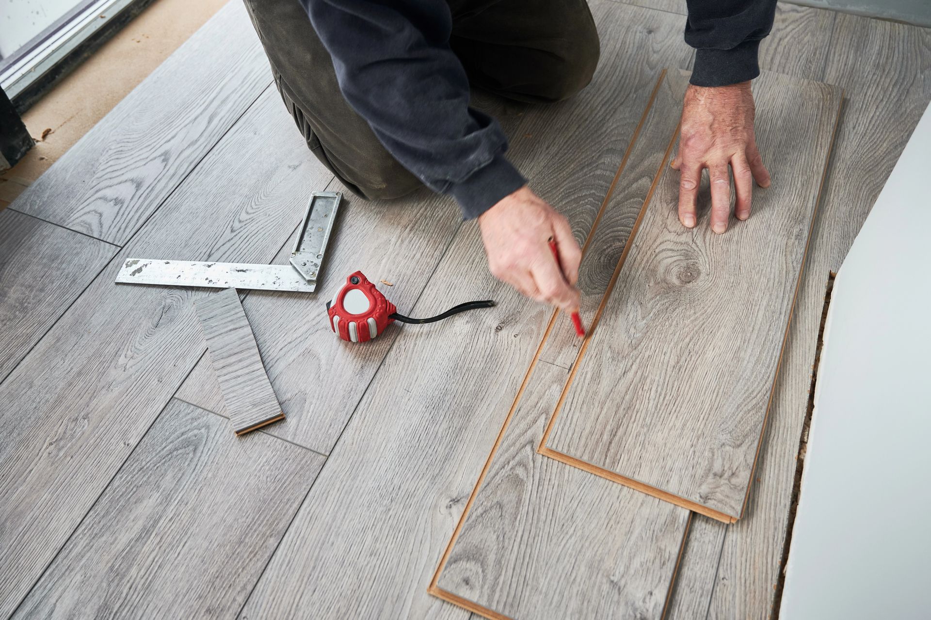 Persona che installa pavimenti in legno utilizzando strumenti di misurazione.